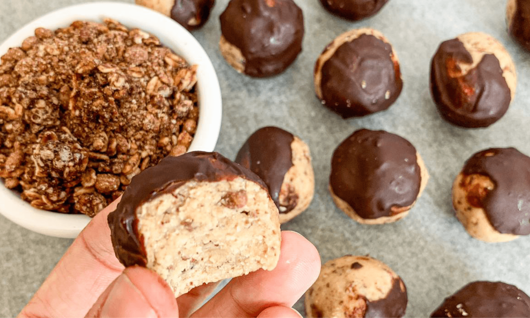 Dark chocolate covered protein balls with crunchy mix & hand in background 